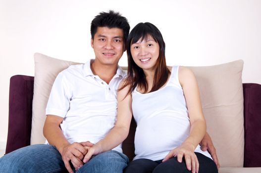 Husband and 8 months pregnant wife sitting on sofa.