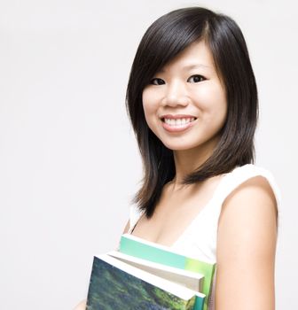 A young Asian girl standing with books.
