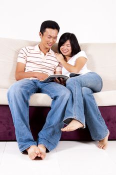 Asian couples sitting on sofa sharing a book.