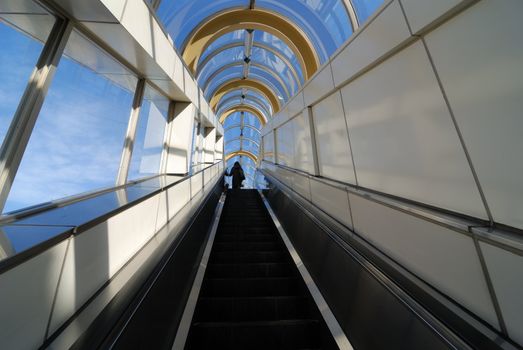 modern building interior with glass roof, moving escalator and woman's figure on the top