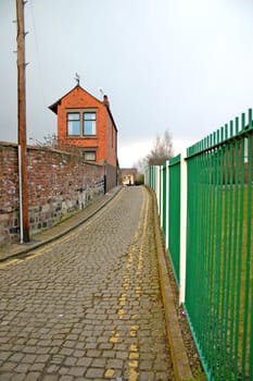 Narrow Cobbled Lane Running Between Metal Fence and House Wall