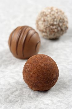Three chocolate truffles on textured paper.  Very Shallow depth of field, focusing on first truffle.
