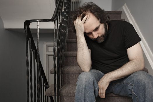 Depressed adult male sitting on stairs. De-saturated slightly for even sadder look.