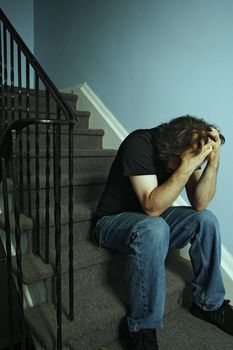 Depressed adult male sitting on stairs. Cross-processed and darkened for moody look.
