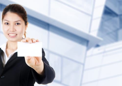 Young Asian with blank business card in a hand, office building as background.