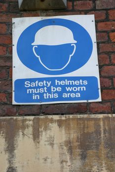 Safety Helmets Must Be Worn in this Area Sign on Brick Wall