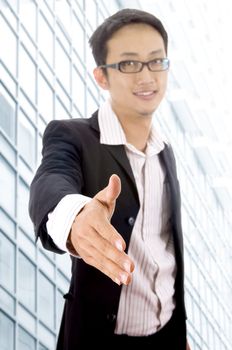 Asian Businessman offering for handshake, office building as background.