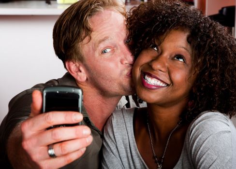 Caucasian man and African American woman taking picture in coffee house with cell phone