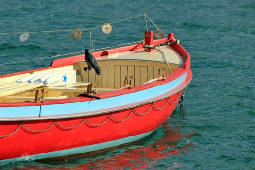 Small red, blue and clear brown wood boat floating on the water by sunny day