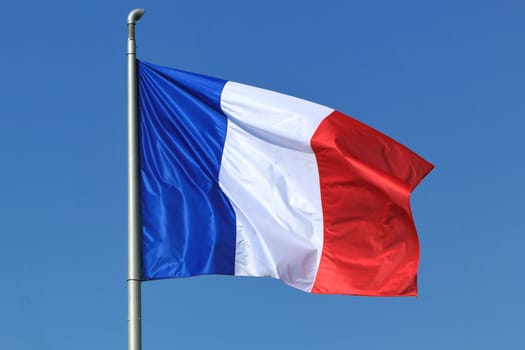 Blue, white and red french flag floating in the wind in a deep blue sky background