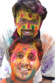 Two young guys with their faces tradiitionally painted in colorful powders, on the occasion of holi festival in India.