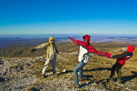 Happy hikers wave their hands and playing with strong wind on mountain summit