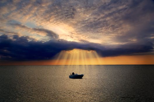 Lonely boat floating in sea is lit by divine light from dark cloud during sunset