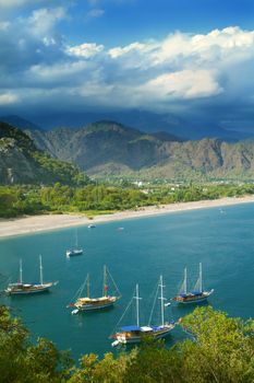Mountainous sea coast with colourful sailboats in cloudy weather