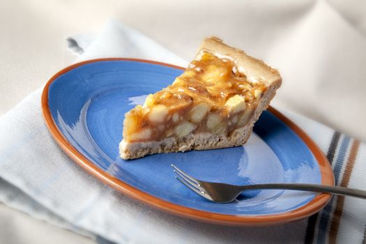 Slice of fresh apple pie on a blue plate with fork.