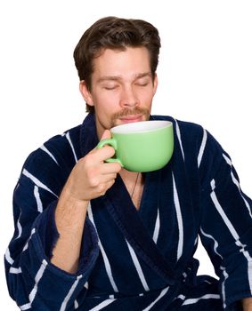 Young man in blue striped bathrobe enjoys his morning cup of tea isolated on white
