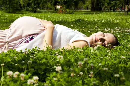 Beautiful pregnant woman relaxing on grass, in the summer park