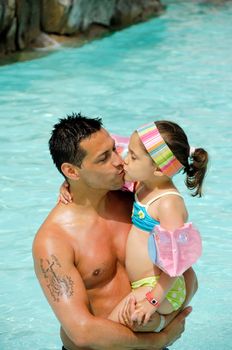 Father and daughter in pool giving eachother a kiss.