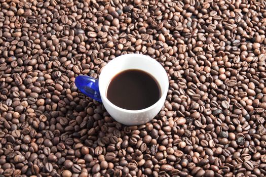 A cup full of coffee surrounded by other coffee beans