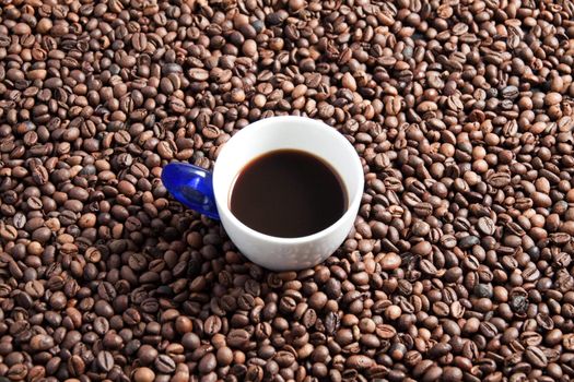 A cup full of coffee surrounded by coffee beans