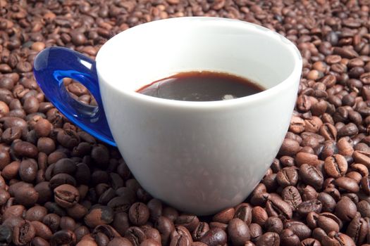 A cup full of coffee surrounded by coffee beans