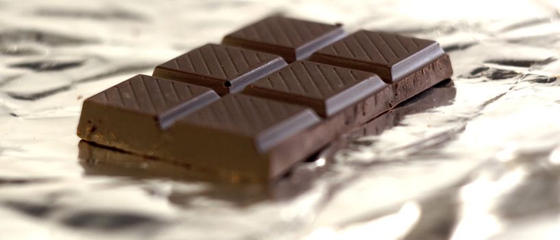 A dark chocolate tablet, on silver paper background