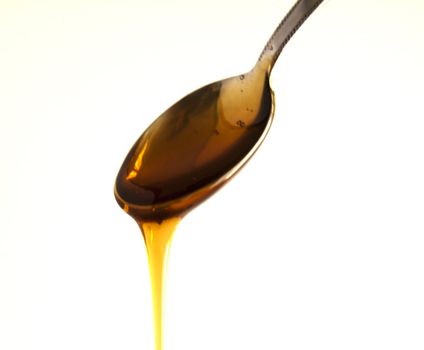 Honey falling from a metal spoon, white background