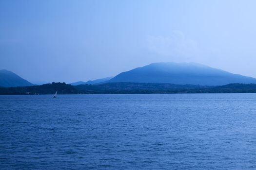 Blue landscape of lake with dark mountains and sails in the background 