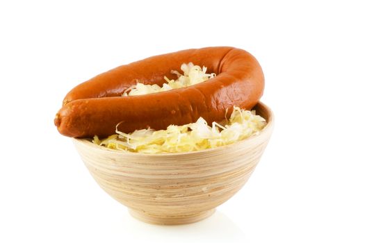 Wooden bowl with sauerkraut and a smoked sausage on a white background.              