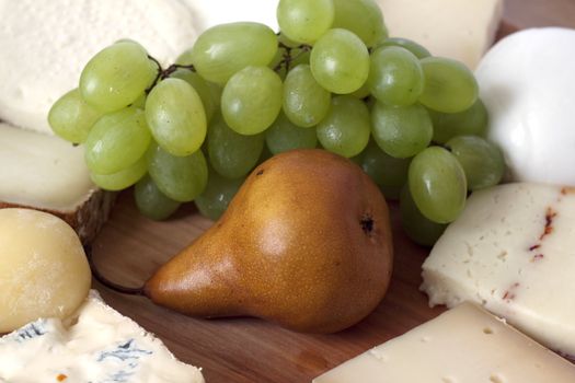 Wooden plate with fruits and several kinds of cheese and bread