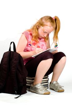schoolgirl sitting on a stack of books making homework