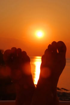 orange sun rising above a sea over crossed feet