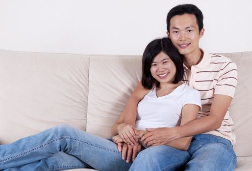 Young Asian couple sitting on sofa with smiling face.