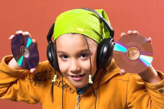 little pretty child listening music in headphones and holding two CD 