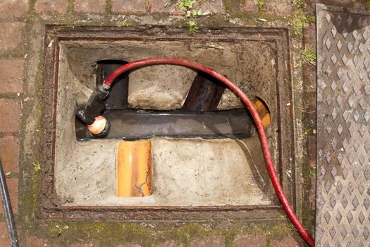 A hose pipe coils into the pipes of an open drain shaped from concrete with a rusty metal rim.