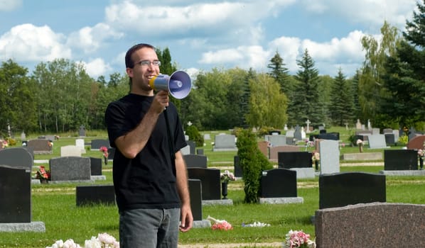 Concept image of the saying, "Don't wake up the dead", featuring a young man talking into a megaphone and standing in a graveyard