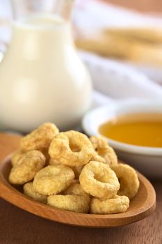 Honey flavoured cereal loops on wooden spoon with milk and honey in the back (Selective Focus, Focus on the front of the loops in the front)