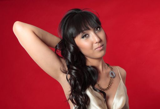 An alluring young woman wears a silk gold dress and necklace accessory.  Red background.