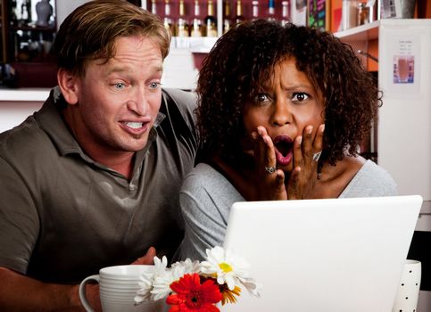 Caucasian man and African American woman in coffee house with laptop computer