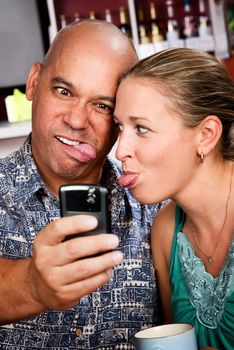 Attractive couple in a coffee house taking self-portrait with cell phone