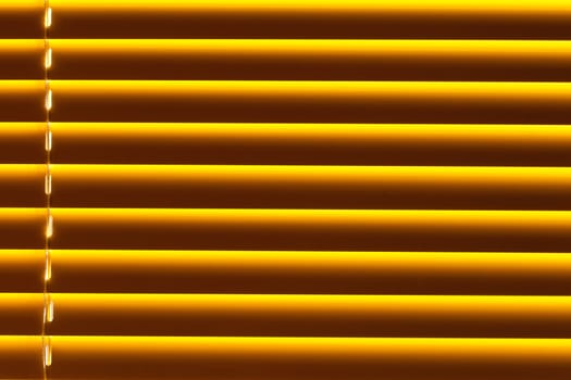 Background pattern texture of yellow plastic blind blocking out bright sunlight shining through window.