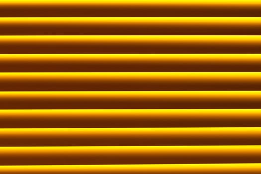 Background pattern texture of yellow plastic blind blocking out bright sunlight shining through window.