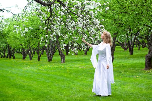 Tne blonde girl in white dress and apple-tree with white flowers
