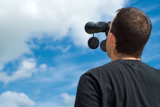 Low angle view of a bird watcher using binoculars with some blue sky and clouds behind him