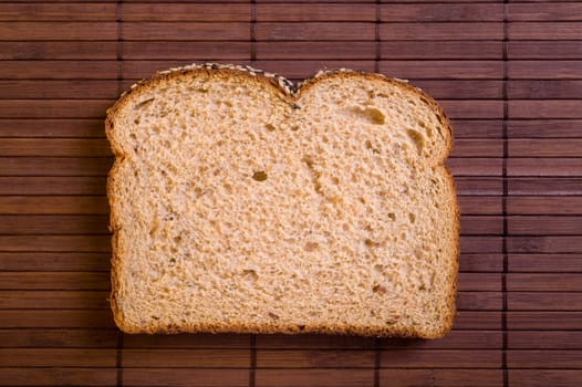 Slice of fresh wholemeal bread, on bamboo mat, studio shot.