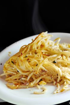 appetizing baked spaghetti on white plate with smoke over black background