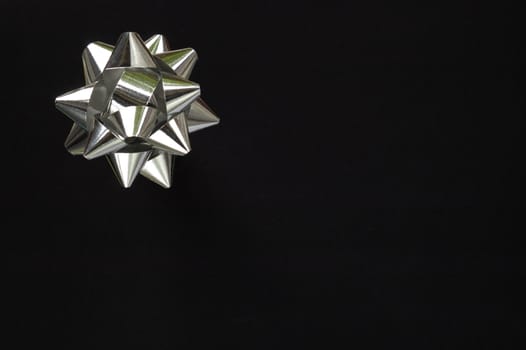 A decorative star, made from silver ribbon, on a pure black background with space for text (copy).