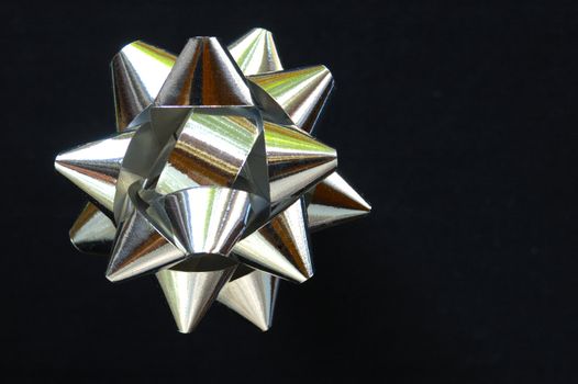 A decorative star, made from silver ribbon, on a pure black background with space for text (copy).