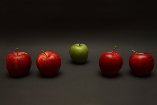 A line of apples, with one red one out.