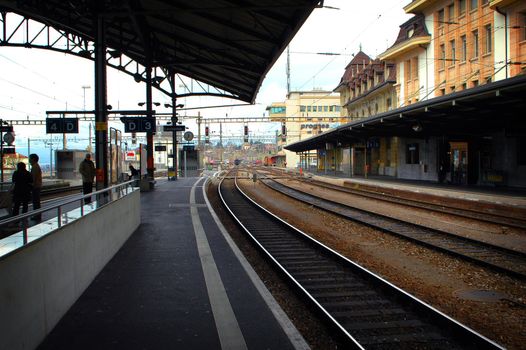 Lausanne Train Station showing train in distance, tracks and people.
